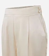 Pantalón de satén color crema, corte carrot, con cintura alta, pliegues, bolsillos laterales y cierre con cremallera.