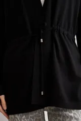 Ruana negra de tejido de punto, con mangas largas y cordón ajustable en la cintura.