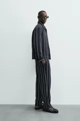 Sobrecamisa de hombre, corte relajado, color azul marino con rayas verticales blancas. Presenta cuello solapa, manga larga con puños abotonados, bolsillos de parche delanteros y cierre frontal de botones.