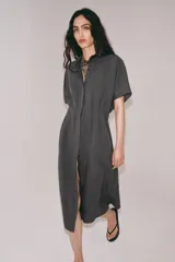 Vestido midi de corte camisero color gris, confeccionado con mezcla de lyocell y lino. Presenta cuello solapa, manga corta, pliegues en la cintura y cierre frontal con botones ocultos.