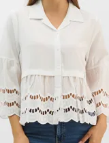 Camisa negra de poliéster con cuello camisero, escote en V y cierre frontal de botones. Cuenta con mangas anchas de corte acampanado y detalles de bordado suizo calado en las mangas y en el ruedo inferior.