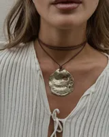 Collar artesanal con dije central de metal con textura orgánica irregular que evoca una ostra. El dije está montado sobre un cordón de algodón natural, permitiendo un uso versátil y regulable.