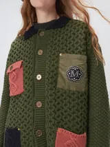 Campera tejida de punto grueso en color beige, con cuello en contraste color verde. Presenta cierre frontal con botones, bolsillos delanteros con apliques en nylon color marrón y bordado decorativo, y forro interno de nylon.