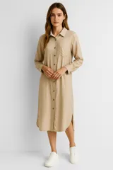 Túnica color beige de lino, de corte holgado, con cuello camisero, cierre frontal con botones, manga larga y bolsillo en el pecho.