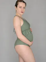 Malla enteriza maternal color verde salvia con tejido texturado, escote con aberturas y volado bajo el busto, de tiro alto diseñado para la etapa de embarazo.