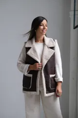 Chaleco de cuero sintético color chocolate con interior y bordes de corderito beige. Presenta solapas amplias, dos bolsillos frontales con detalle de corderito y corte recto.