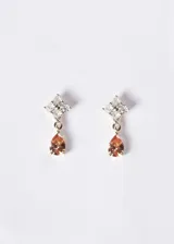 Par de aros colgantes de plata 925 con baño de oro de 18k, compuestos por un diseño superior de cuatro zirconias blancas en forma de flor y un dije colgante en forma de gota de zirconia color anaranjado.