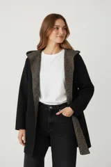 Saco largo negro con capucha, de corte holgado. El forro interior y el borde de la abertura frontal y la capucha tienen un estampado geométrico en tonos marrón y beige.