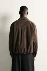 Cazadora de corte relajado color marrón, confeccionada en tejido de algodón. Presenta cuello solapa, cierre frontal con botones, bolsillo plastrón en el pecho, bolsillos laterales de vivo y bajo ajustable con elástico en los laterales.