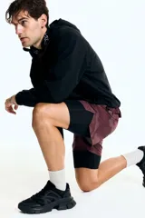 Short deportivo de doble capa, con calza interior. El short exterior es de color borgoña con un estampado sutil de puntos en forma de camuflaje. Posee cintura elástica con cordón oculto y aberturas laterales. La calza interior es negra.