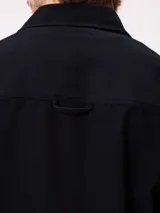 Camisa de gabardina color verde oliva, con cuello clásico, cierre frontal de botones y dos bolsillos frontales con parche. Incluye un pequeño parche con el logo de la marca en el bolsillo izquierdo.