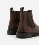 Bota tipo Chelsea de caña media, confeccionada en cuero sintético color marrón oscuro. Presenta punta redonda, paneles laterales elásticos para facilitar el calce y suela de goma robusta.