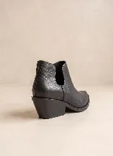 Botín de cuero vacuno color negro, con diseño de corte lateral y taco cuadrado de 5 cm. Presenta punta fina y suela de caucho antideslizante.