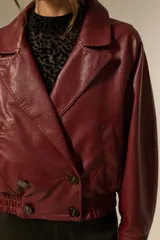 Campera estilo biker de eco-cuero color bordó, con cuello solapa ancho, manga larga y calce holgado. Presenta cierre frontal y botones decorativos en la parte inferior delantera.