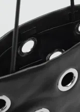 Bolso tipo shopper de color negro con diseño de ojales metálicos plateados. Cuenta con doble asa de hombro y cierre de botón magnético.