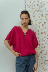 Blusa de lino color fucsia, con escote en V y manga corta amplia. Presenta un detalle de botón decorativo dorado en el centro del escote.