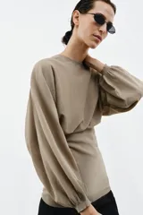 Cuerpo de punto con cuello redondo y mangas largas abullonadas. Presenta un diseño con cintura entallada y bajo ajustado.