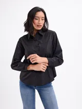 Camisa blanca de manga larga con cuello camisero, cierre frontal con botones y detalles de tablas verticales en el frente.