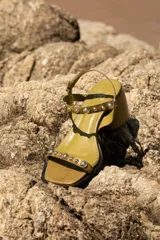 Sandalia de cuero color bronce metalizado, con punta cuadrada, taco ancho y bajo, y tiras finas adornadas con tachas esféricas plateadas.