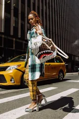 Mochila Sprayground mediana unisex, de cuero vegano con estampado a cuadros marrón y gris. Presenta un diseño de boca de tiburón con dientes blancos y encías rojas.