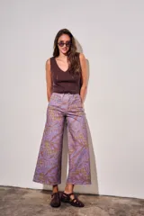 Pantalón jean de tiro alto y corte wide leg, con estampado de hojas grandes en tonos morados y fondo con patrón a cuadros.