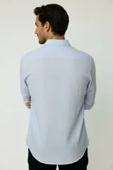 Camisa de algodón celeste claro, de corte holgado, con mangas largas, cuello camisero y cierre frontal con botones.