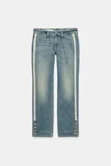Jeans rectos de tiro medio en denim azul con efecto deslavado. Presentan bandas laterales con detalles brillantes, bolsillos delanteros y traseros, y aberturas en los tobillos con botonadura metálica.