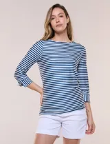 Remera de agua de silueta estilizada confeccionada en tejido técnico elastizado con protección solar UPF 50, con escote barco amplio y mangas 3/4 terminadas con puño en rayas verticales a contraste con pequeña abertura. Presenta aberturas laterales en el bajo decoradas con botones dorados grabados y ruedo recto de calce cómodo.