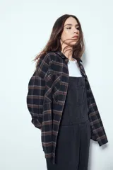 Camisa tipo leñadora de corte oversize, con estampado de cuadros en tonos negro y marrón. Presenta cuello clásico, cierre frontal con botones y mangas largas con puños abotonados.