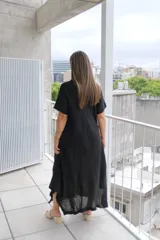 Vestido largo negro de manga corta, con corte acampanado y bajo asimétrico con detalle deshilachado en picos desiguales.