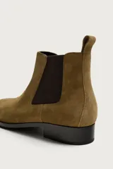 Bota Chelsea de gamuza color tostado, con paneles elásticos laterales en marrón oscuro, punta redonda y suela plana con pequeño tacón.