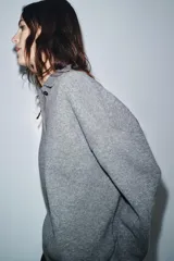 Sweater de punto liso color gris melange, con cuello polo, manga larga y cierre frontal con botones. Presenta puños y ruedo acanalados.