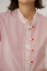 Blusa celeste a rayas blancas, de manga corta abullonada. Cuenta con cuello mao y tapeta de botones con detalles de estampado floreado en tono rosado, presentes también en el cuello y los puños.