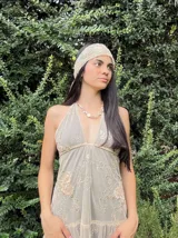 Vestido corto negro con escote en V profundo, estilo halter con tiras para atar al cuello. Presenta un diseño ajustado en el busto con tiras ajustables bajo el mismo que se cruzan y anudan en la espalda, y falda con volado en el ruedo con detalle de encaje.