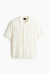 Camisa de punto acanalado color blanco, con cuello camisero, manga corta y cierre frontal con botones.