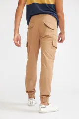 Pantalón cargo de corte slim, color verde oliva, con bolsillos laterales tipo cargo, cierre frontal con botón y puños elásticos en los tobillos.