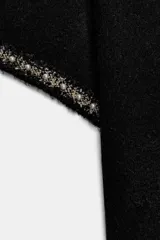 Jersey de punto negro de cuello redondo y manga corta, con detalle de perlas decorativas en el borde de las mangas.