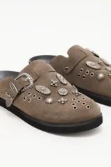 Zueco de cuero descarne negro con diseño de estilo western, decorado con tachas metálicas plateadas y una hebilla lateral ajustable.