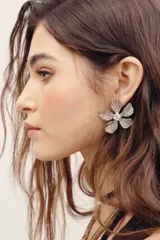 Aros con diseño de flor de metal plateado con textura y un cristal transparente en el centro.