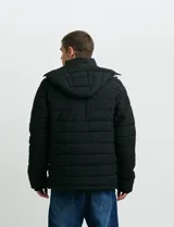 Campera puffer verde militar de cuello alto, con cierre frontal y solapa con broches a presión. Cuenta con bolsillos laterales y un bolsillo vertical en el pecho con cierre, ambos con tiradores naranjas.