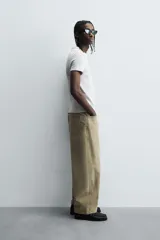 Camiseta de corte relajado, color gris claro, confeccionada en tejido con estructura waffle. Presenta cuello redondo y manga corta, con costuras decorativas en contraste color dorado que recorren los laterales y los hombros.