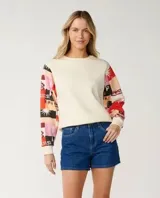 Buzo de cuello redondo color off white, con mangas largas estampadas con diseño patchwork multicolor en tonos rojos, rosas y negros.