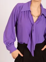 Blusa negra de manga larga con cuello camisero y lazo frontal. Presenta frunces en los hombros y puños ajustados con elástico.