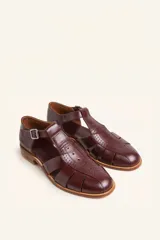 Sandalia cerrada tipo pescador de cuero negro charol, con tira en T y hebilla ajustable en el tobillo. Posee suela y taco bajo de madera.