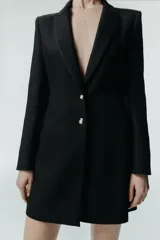 Blazer larga negra con cuello solapa, manga larga y bolsillos de vivo en el delantero. Cierre frontal con dos botones plateados.