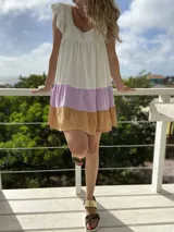 Vestido corto de lino color blanco con falda escalonada en lila y ocre. Tiene escote cuadrado, mangas cortas con volados y corte holgado.