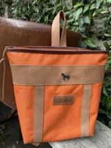 Mochila de lona roja con detalles y correas de cuero marrón, cierre superior y aplique metálico con forma de caballo.