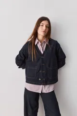 Sobrecamisa de jean azul oscuro, de calce relajado, escote en V, bolsillos delanteros aplicados, cierre frontal con botones metálicos y pespuntes en contraste.