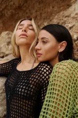Vestido corto de tejido crochet calado en color negro, con mangas largas y diseño de espalda descubierta con cierre de lazo ajustable en el cuello.