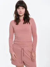 Remera de manga larga entallada, confeccionada en tejido pointelle con textura acanalada. Presenta escote bote con un delicado detalle de lazo pequeño y bordado en el centro del pecho.